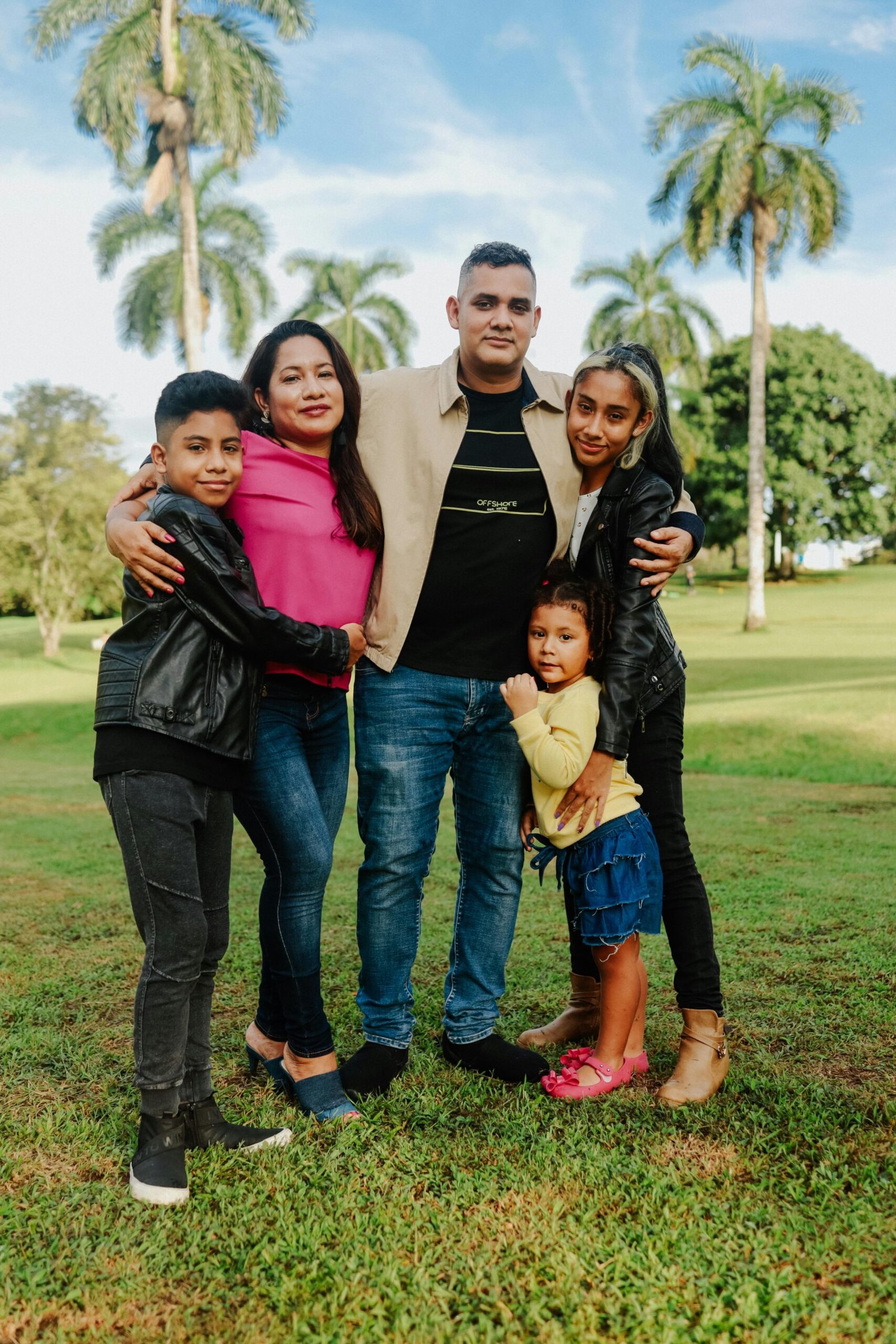 Family of five enjoying a sunny day at the park, surrounded by palm trees and greenery.