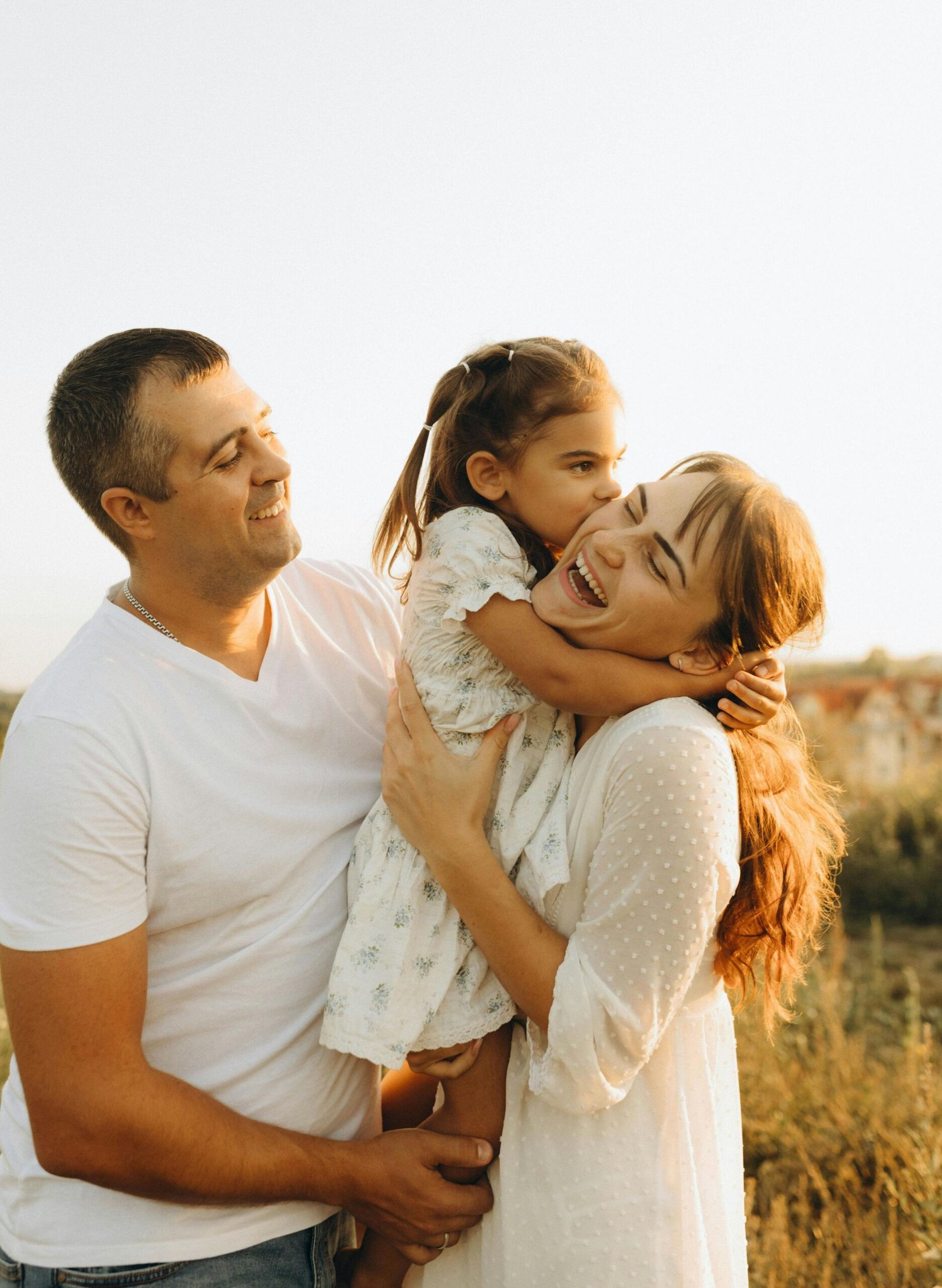 A joyful family moment with parents holding their daughter outdoors during sunset.